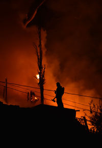 Low angle view of silhouette fireman against sky during fire