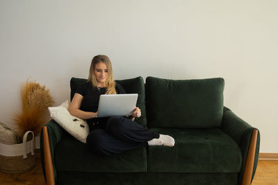 Woman working at home from couch with laptop on her lap. home office concept. gray notebook