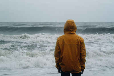 Rear view of man standing on beach against sky