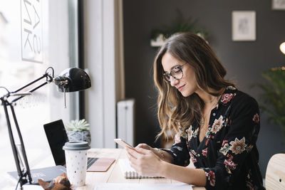 Young woman using phone while sitting on table