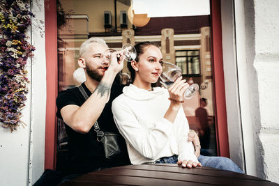 Young man and woman holding glass while standing outdoors