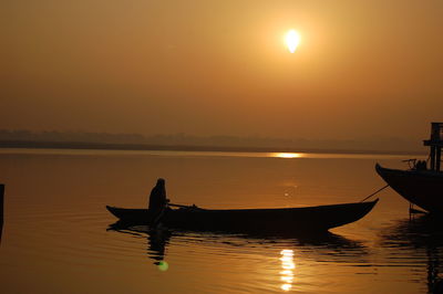 Silhouette boat moored on sea against sky during sunset