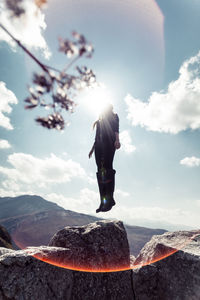 Low angle view of woman levitating on rock against sky