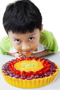 Portrait of boy with tart on table against white background