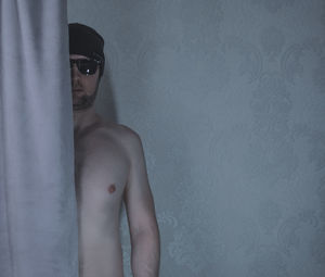 Portrait of young man looking away while standing against wall