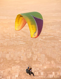 Person paragliding against sky in city