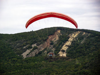 Woman parachuting over mountain against sky