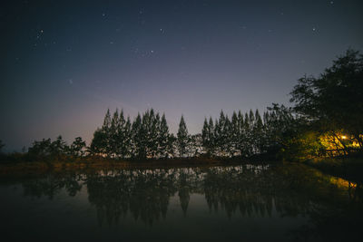 Reflection of trees in lake against sky at night