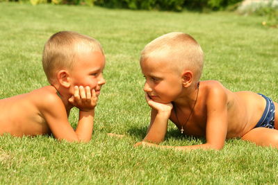 Two boys, brothers have a rest on a green grass, in the summer