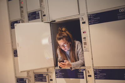 Young woman using phone in locker