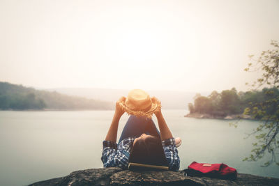 Woman sitting by lake against clear sky