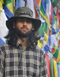 A bearded and long haired male tourist  looking at camera, standing against buddhist prayer flags