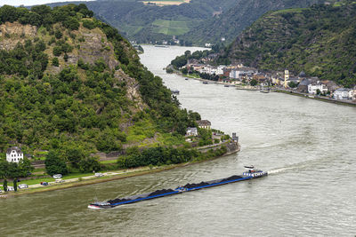 A barge with coal sailing on the river rhine in western germany, visible buildings on the river bank