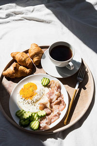 Breakfast in bed coffee cup, fried egg, bacon and croissants on wooden tray. 