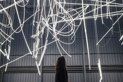 Rear view of woman standing on illuminated walkway at night