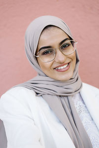 Smiling woman wearing eyeglasses standing in front of pink wall