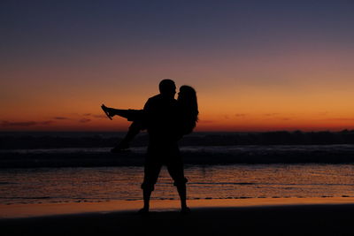 Silhouette couple at beach against orange sky during sunset