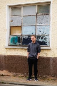 Portrait of young man standing against window outdoors