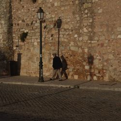 Rear view of woman walking on street against wall