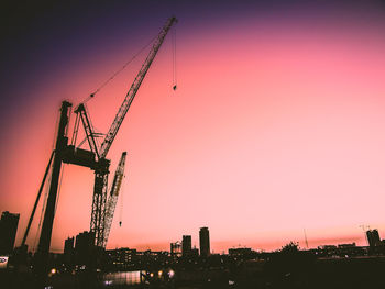 Silhouette cranes at construction site against sky during sunset