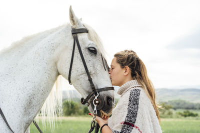 Young woman kissing white horse at countryside