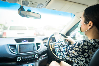 Young woman wearing medical face mask to preventing flu, pollution and convid 19 while driving.