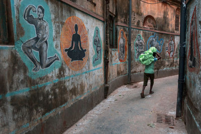 Rear view of man walking against graffiti wall