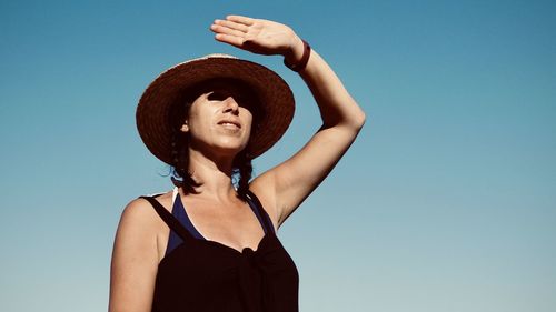 Low angle portrait of woman standing against clear blue sky
