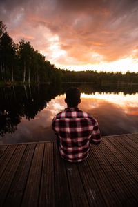 Rear view of man looking at lake against sky