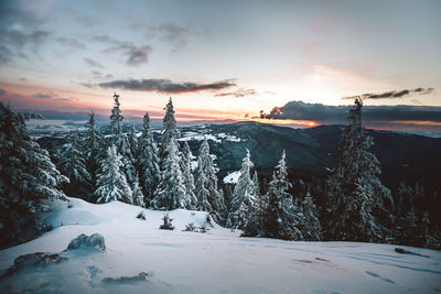 Snow covered land against sky during sunset