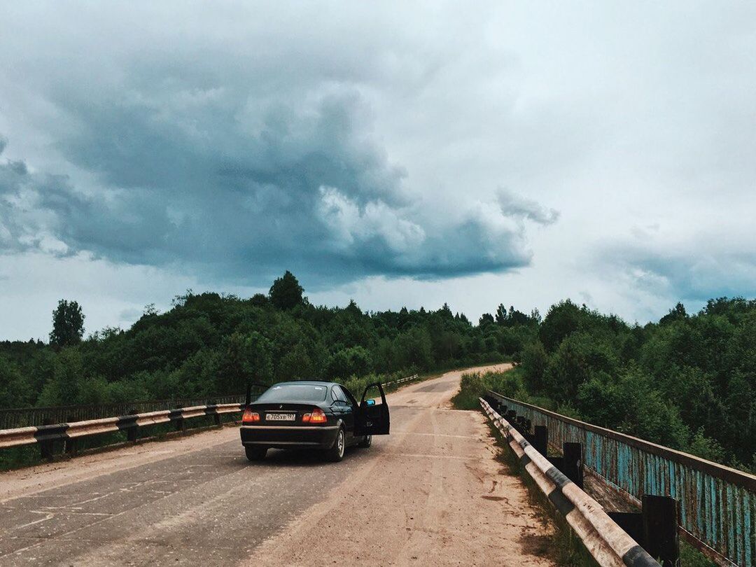 CAR MOVING ON ROAD AGAINST CLOUDY SKY