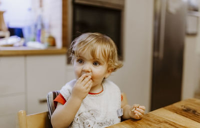 Cute baby boy sitting by table on chair at home