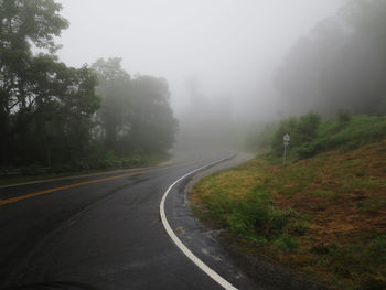 Empty road along trees and plants against sky