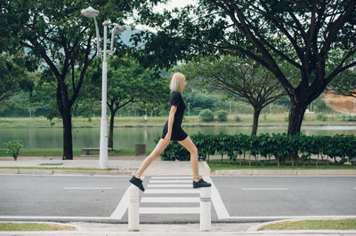 Side view of young woman standing on bollards at footpath