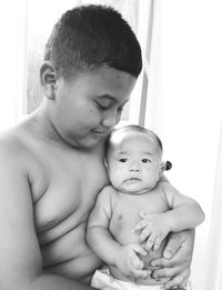 Shirtless boy holding baby at home