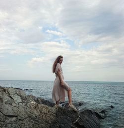 Woman standing on rock by sea against sky