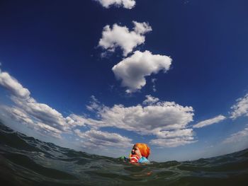 Fish-eye lens view of girl swimming in sea against blue sky