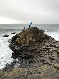 People on rocks at beach by sea against sky