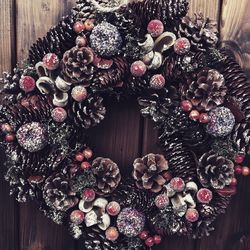 Close-up of wreath with pine cones and decorations hanging on wooden wall