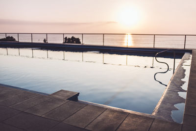 Swimming pool by sea against sky during sunset