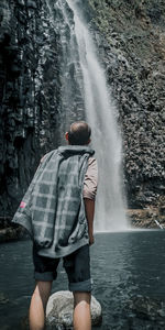 Rear view of man standing at waterfall in forest
