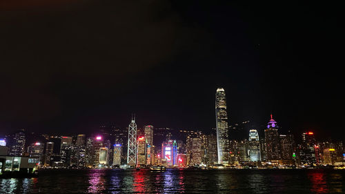 Illuminated buildings by river against sky at night