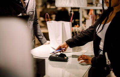 Midsection of female customer paying through smart phone at store