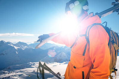 Shot of a skier standing on top of a mountain with skis on his shoulder on a sunny winter day