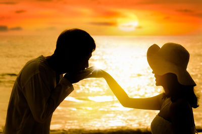 Side view of mother and daughter standing on beach during sunset