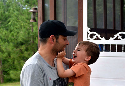 Father carrying playful son outside house