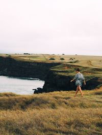 Rear view of woman walking on field against sky