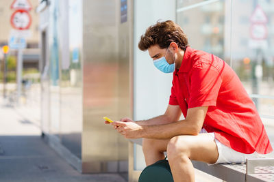 Side view of young man using mobile phone sitting outdoors