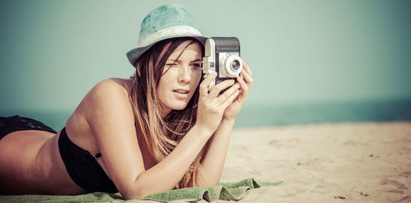 Young woman photographing with camera while lying on sand at beach