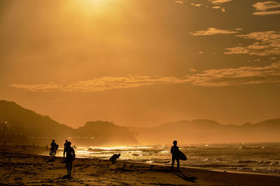 Silhouette people on beach against sky during sunrise